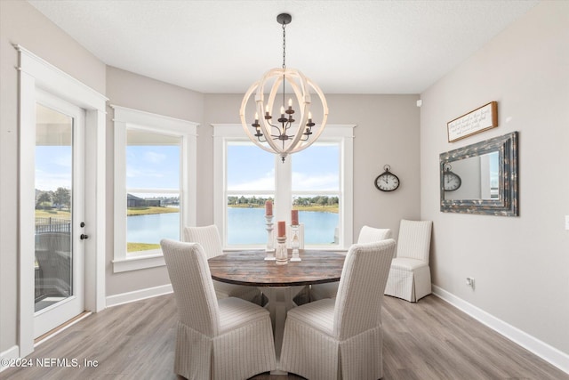 dining area featuring light hardwood / wood-style floors, a water view, a textured ceiling, and a chandelier