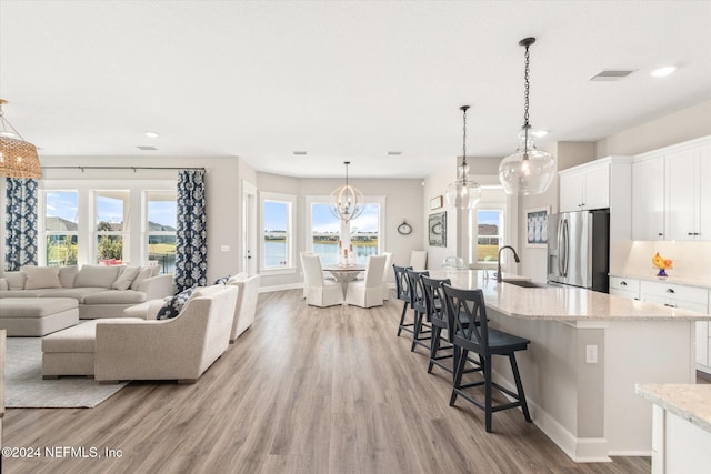 kitchen with stainless steel refrigerator with ice dispenser, white cabinetry, hanging light fixtures, and sink