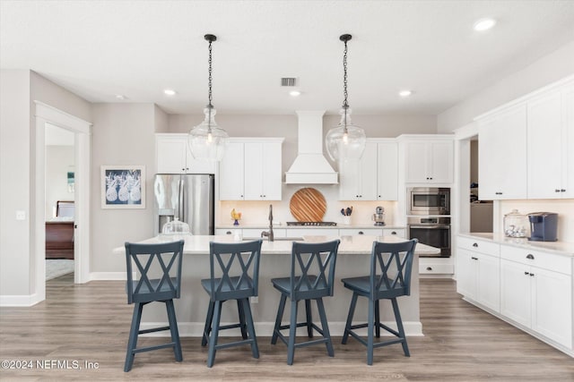 kitchen with a center island with sink, decorative light fixtures, custom range hood, and stainless steel appliances