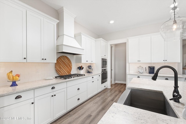 kitchen with light stone countertops, appliances with stainless steel finishes, custom range hood, sink, and white cabinets