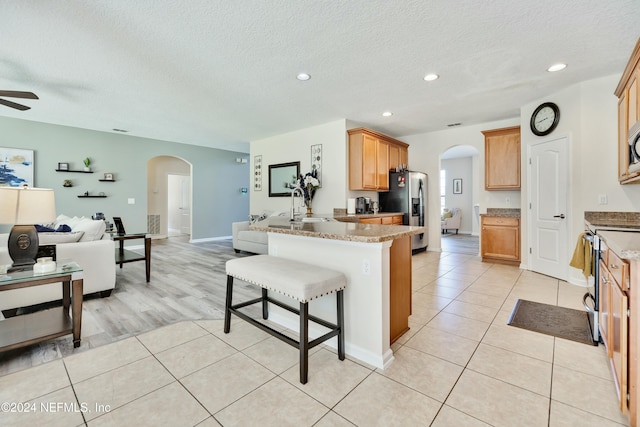 kitchen with a breakfast bar, ceiling fan, light stone counters, kitchen peninsula, and stainless steel appliances