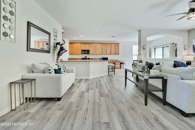 living room featuring a textured ceiling, ceiling fan, light wood-type flooring, and sink