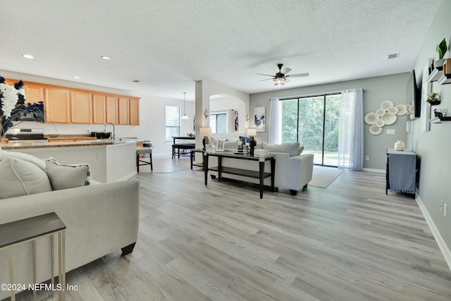 living room with a textured ceiling, light hardwood / wood-style flooring, and ceiling fan