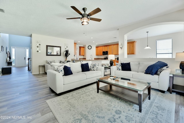 living room featuring ceiling fan, sink, light hardwood / wood-style floors, and a textured ceiling