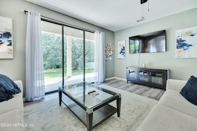 living room with ceiling fan, a textured ceiling, and light hardwood / wood-style flooring