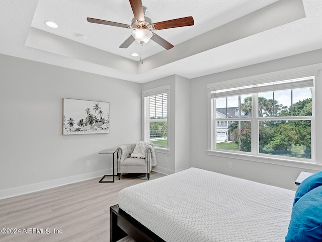 bedroom with light hardwood / wood-style floors, a tray ceiling, a textured ceiling, and ceiling fan