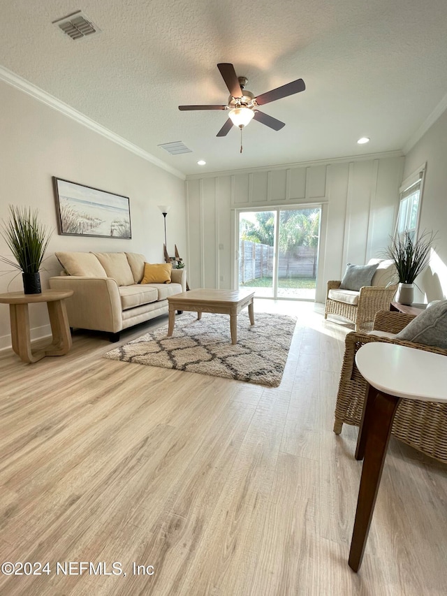 living room featuring ceiling fan, light hardwood / wood-style floors, ornamental molding, and a textured ceiling