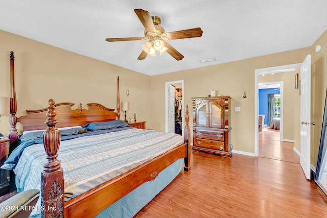 bedroom with ceiling fan, a spacious closet, a textured ceiling, light hardwood / wood-style floors, and a closet