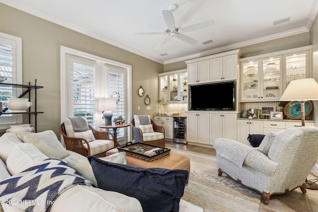 living room with light wood-type flooring, beverage cooler, crown molding, ceiling fan, and bar area