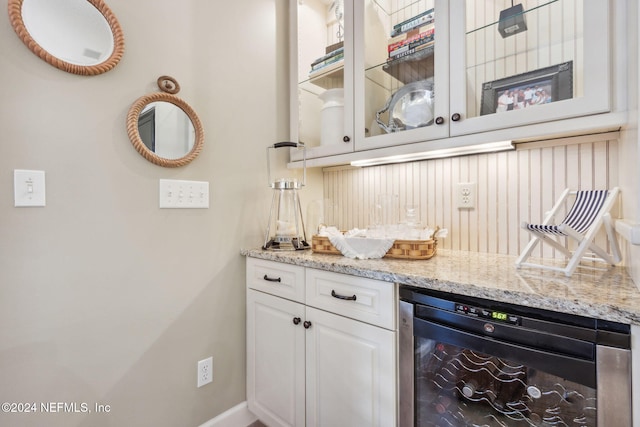 bar with light stone counters, white cabinetry, and beverage cooler