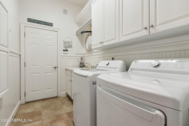 clothes washing area featuring washing machine and clothes dryer, light tile patterned floors, and cabinets