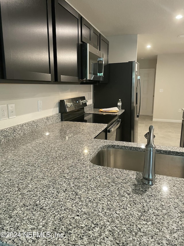 kitchen featuring tile patterned floors, light stone countertops, sink, and appliances with stainless steel finishes