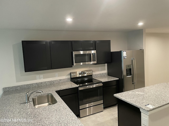 kitchen with appliances with stainless steel finishes, light tile patterned floors, light stone counters, and sink