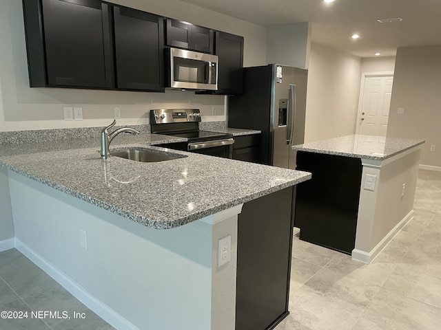 kitchen with light stone countertops, kitchen peninsula, stainless steel appliances, sink, and a kitchen island