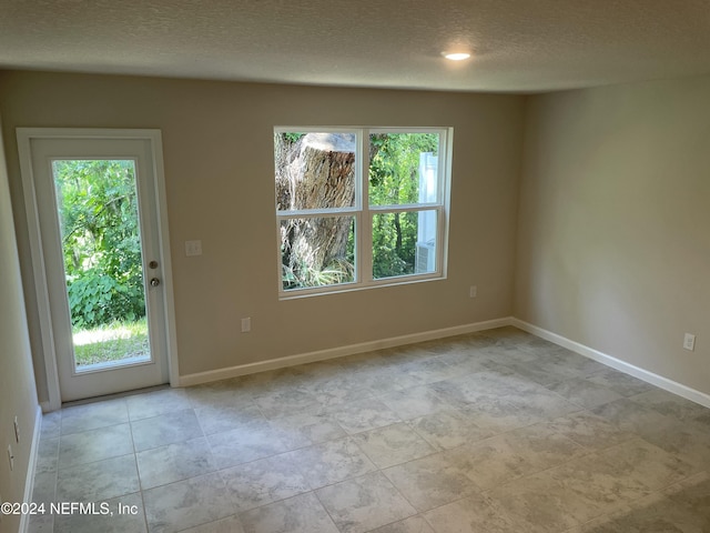 tiled empty room with a textured ceiling and a wealth of natural light