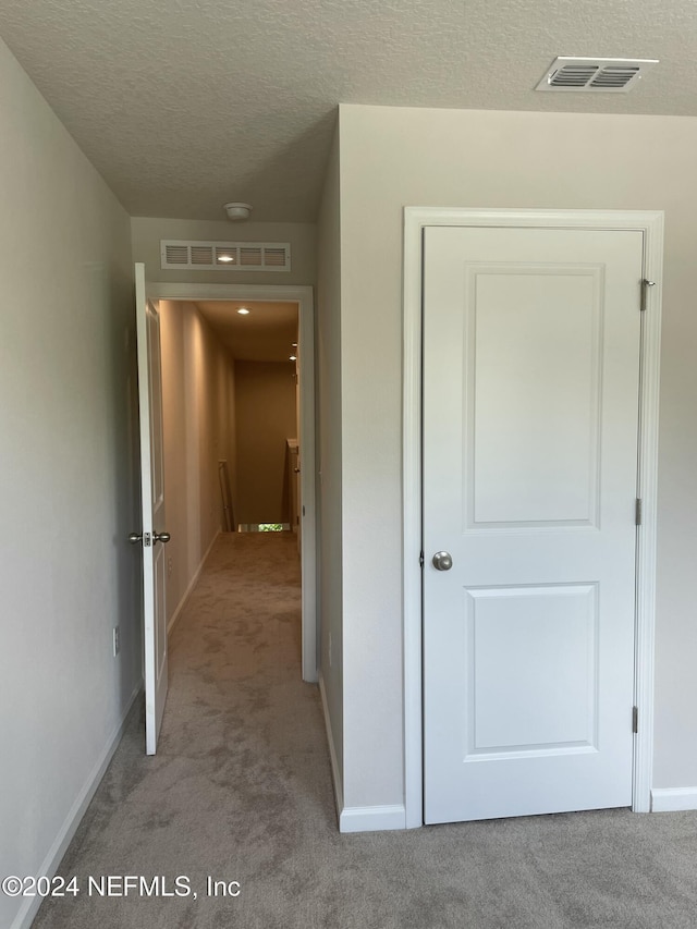 hallway with a textured ceiling and light carpet