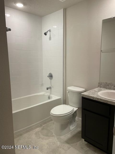 full bathroom with a textured ceiling, vanity, tiled shower / bath combo, and toilet