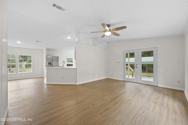 unfurnished living room with a textured ceiling, light hardwood / wood-style flooring, and french doors