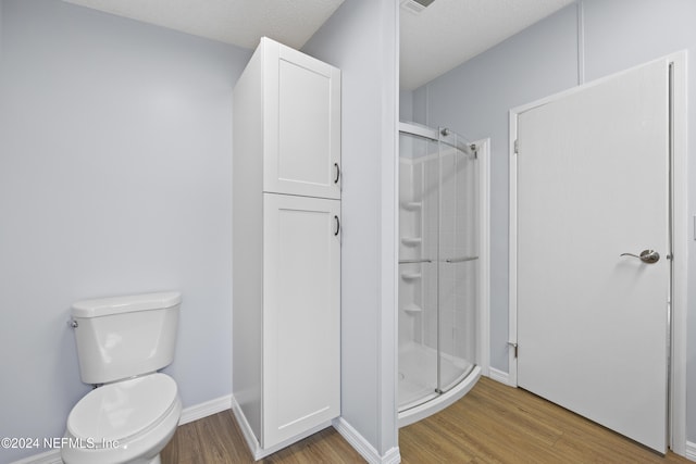 bathroom with wood-type flooring, a textured ceiling, toilet, and walk in shower