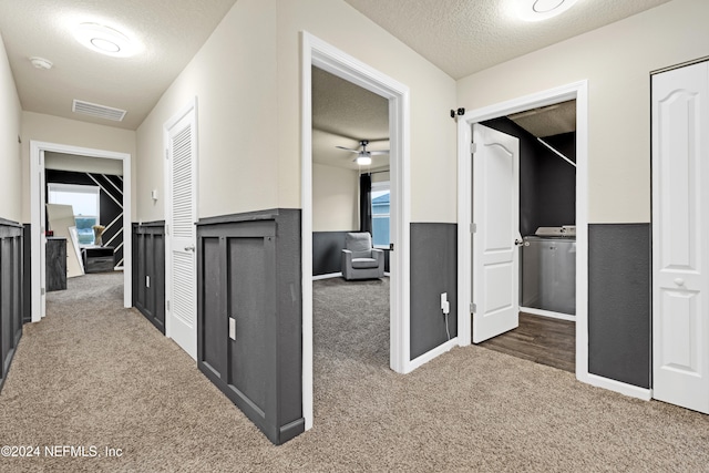 hall featuring a textured ceiling, washer / clothes dryer, dark carpet, and a healthy amount of sunlight