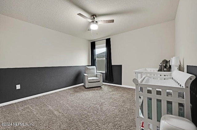 carpeted bedroom featuring a textured ceiling, a nursery area, and ceiling fan