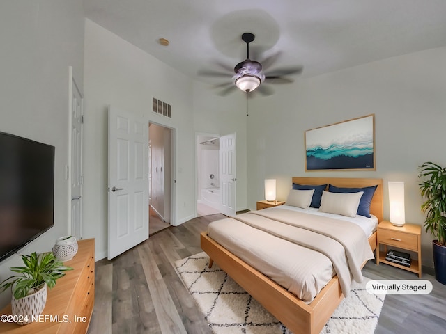 bedroom featuring wood-type flooring, a towering ceiling, ensuite bathroom, and ceiling fan