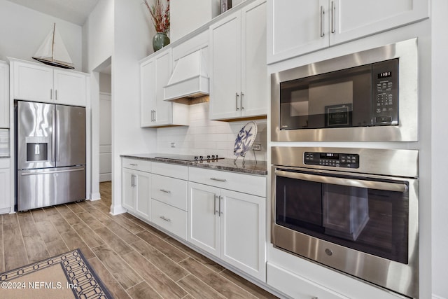 kitchen with appliances with stainless steel finishes, tasteful backsplash, dark stone counters, custom exhaust hood, and white cabinetry