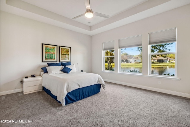 bedroom featuring a raised ceiling, ceiling fan, a water view, and carpet floors