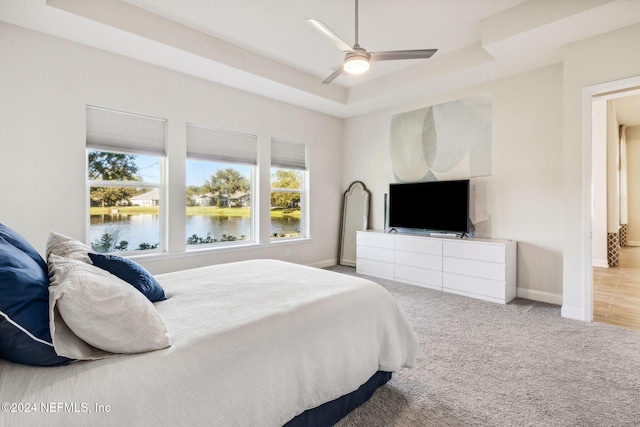 carpeted bedroom with a raised ceiling and ceiling fan