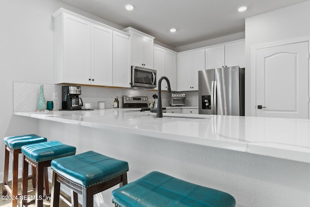 kitchen with a breakfast bar area, kitchen peninsula, white cabinets, and stainless steel appliances