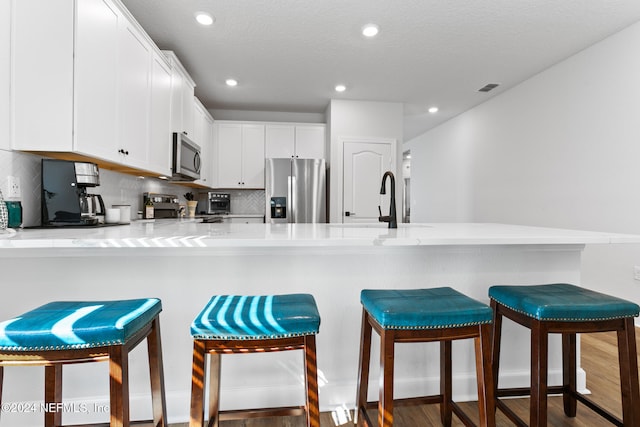 kitchen featuring a breakfast bar area, kitchen peninsula, white cabinets, and appliances with stainless steel finishes