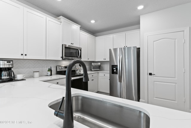 kitchen featuring decorative backsplash, appliances with stainless steel finishes, light stone counters, a textured ceiling, and white cabinets