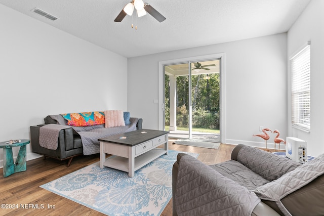 living room with a textured ceiling, ceiling fan, and dark wood-type flooring