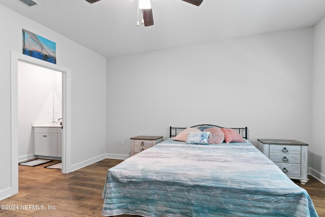 bedroom with a textured ceiling, ceiling fan, dark wood-type flooring, and connected bathroom