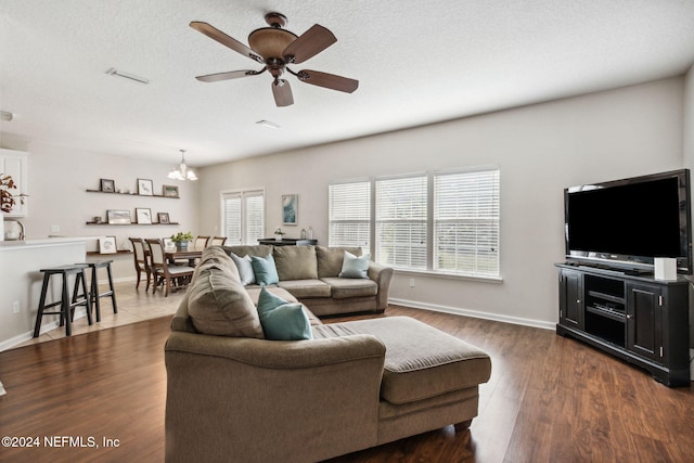 living room featuring a textured ceiling, dark wood-type flooring, and ceiling fan with notable chandelier