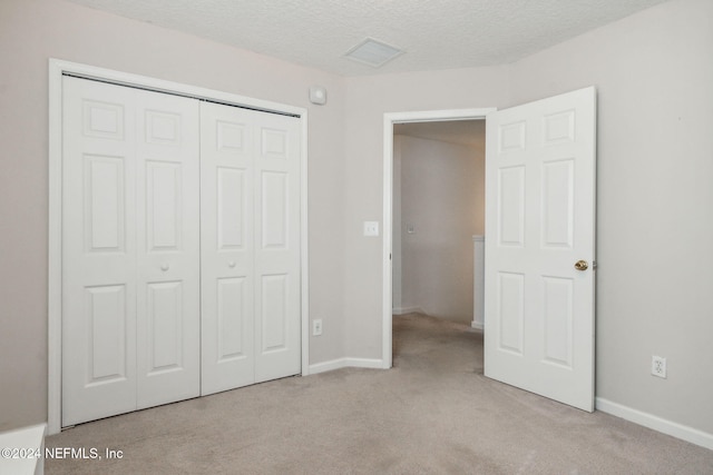 unfurnished bedroom featuring light carpet, a closet, and a textured ceiling