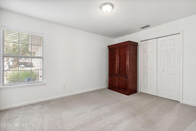 unfurnished bedroom featuring a closet, light colored carpet, and a textured ceiling