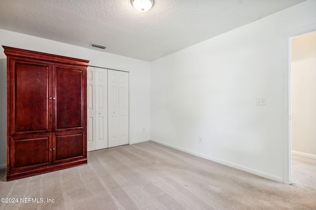 unfurnished bedroom featuring a textured ceiling, light carpet, and a closet