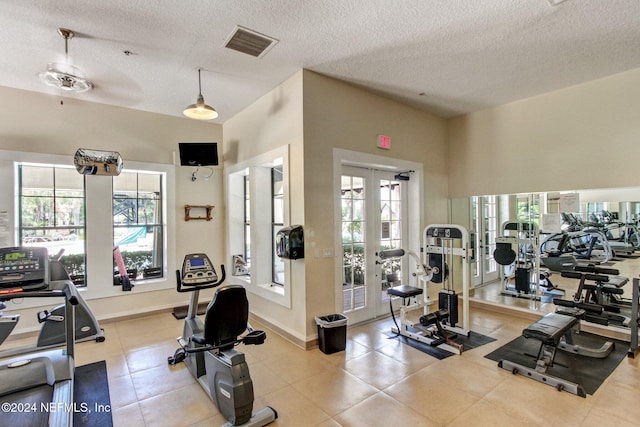 workout area featuring ceiling fan, light tile patterned floors, a healthy amount of sunlight, and a textured ceiling