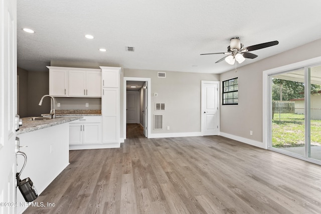 kitchen with white cabinets, ceiling fan, light wood-type flooring, a textured ceiling, and light stone counters