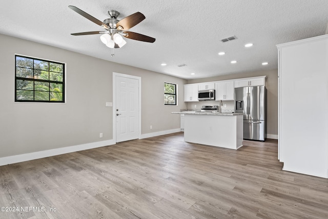 kitchen featuring light stone countertops, white cabinetry, stainless steel appliances, light hardwood / wood-style floors, and a textured ceiling