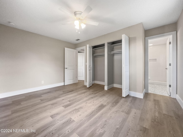 unfurnished bedroom featuring ensuite bath, ceiling fan, light hardwood / wood-style floors, a textured ceiling, and two closets