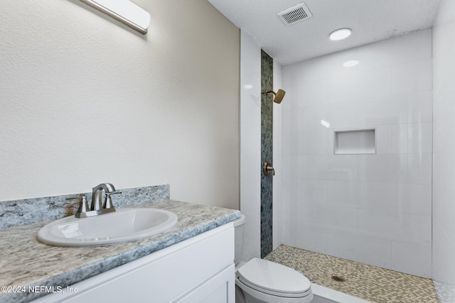 bathroom featuring tiled shower, a textured ceiling, vanity, and toilet