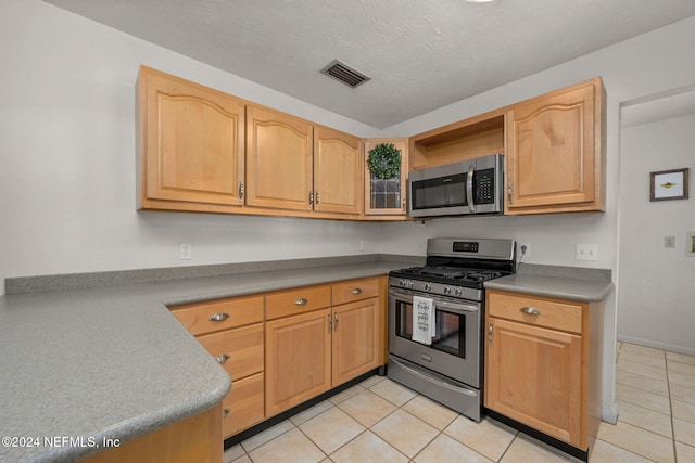 kitchen with light tile patterned floors, light brown cabinets, stainless steel appliances, and a textured ceiling