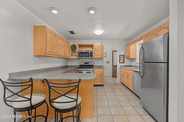 kitchen with a kitchen breakfast bar, kitchen peninsula, stainless steel appliances, and light tile patterned flooring