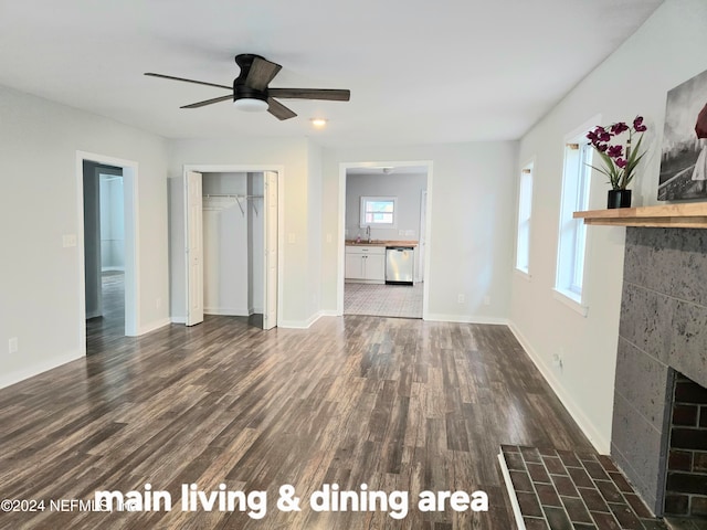 unfurnished living room featuring a tiled fireplace, a wealth of natural light, sink, and dark hardwood / wood-style floors