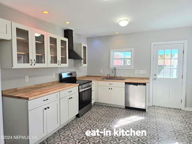 kitchen with white cabinets, wall chimney range hood, sink, butcher block counters, and stainless steel appliances