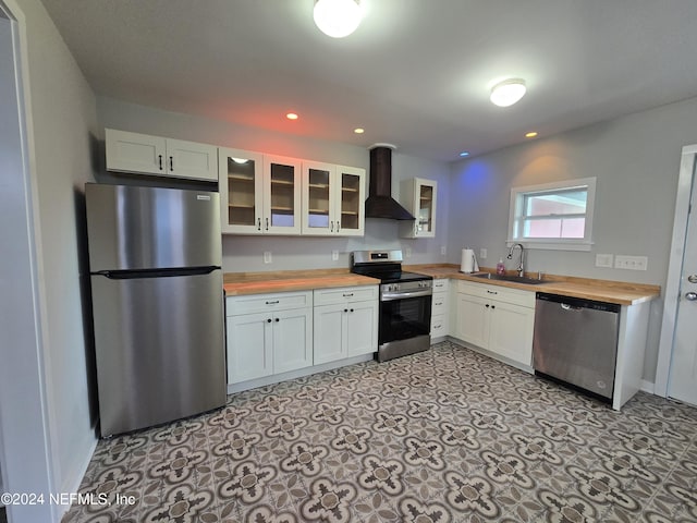 kitchen with butcher block countertops, white cabinets, wall chimney range hood, and appliances with stainless steel finishes