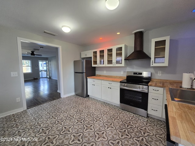 kitchen with ceiling fan, wall chimney exhaust hood, stainless steel appliances, butcher block countertops, and white cabinets