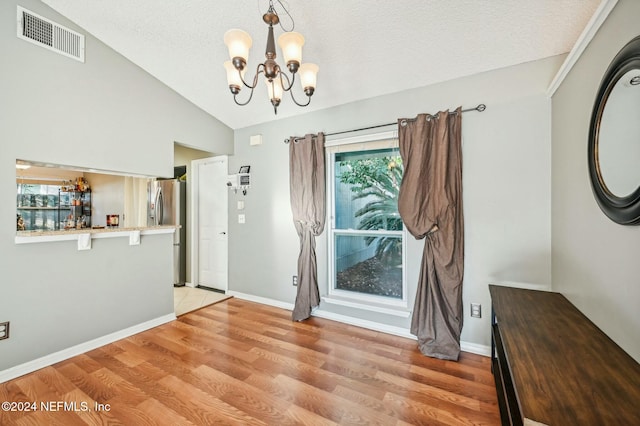 unfurnished dining area featuring a textured ceiling, an inviting chandelier, light hardwood / wood-style flooring, and vaulted ceiling